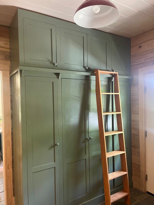 Sage-painted floor-to-ceiling mudroom cabinets with a cherry library ladder